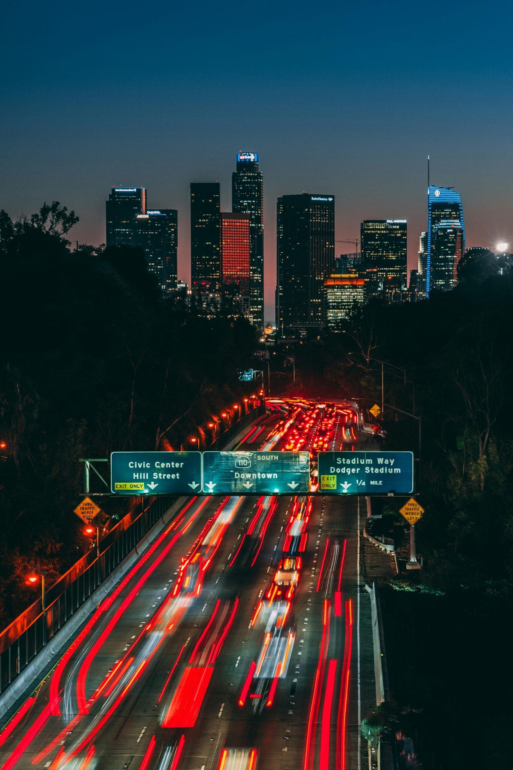 Dynamic Los Angeles skyline at night with light trails on the freeway showcasing urban energy.