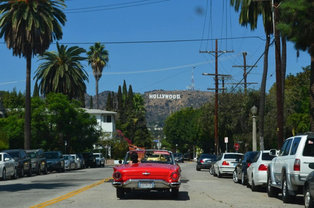 Understanding Heat Pump Costs in Los Angeles 114 Red convertible driving down a sunny street towards the iconic Hollywood sign in Los Angeles.
