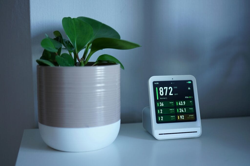pexels-photo-32079712-32079712 A modern air quality monitor next to a green plant on an indoor table, measuring CO2 levels.