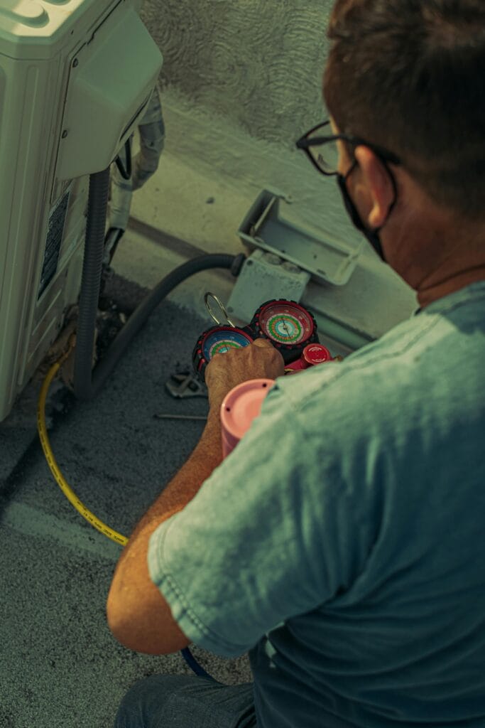 pexels-photo-6471913-6471913 Professional technician repairing an outdoor air conditioning unit with gauges and tools.