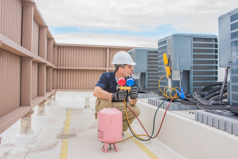 HVAC technician performing rooftop air conditioning maintenance using manifold gauges and refrigerant equipment
